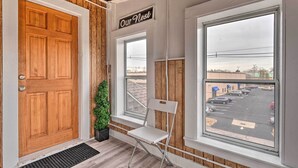Eine Holztür, ein Schild mit der Aufschrift 'Our Nest', ein Fenster mit Blick auf einen Parkplatz und ein weißer Stuhl.
