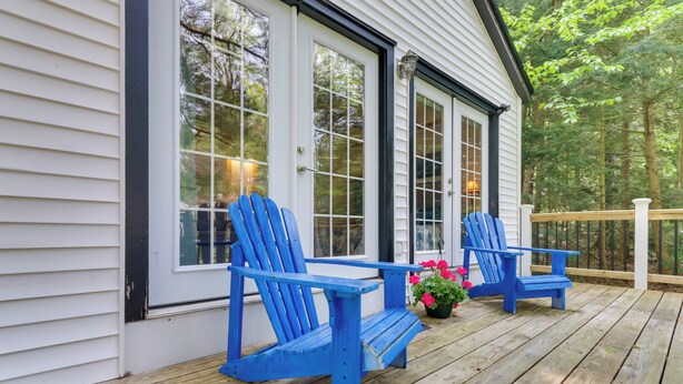 Une terrasse en bois avec deux chaises Adirondack bleues et un pot de fleurs contenant des fleurs roses.