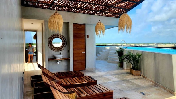 Un balcón moderno al aire libre con sillones de madera, un lavamanos incorporado y vista a una piscina.