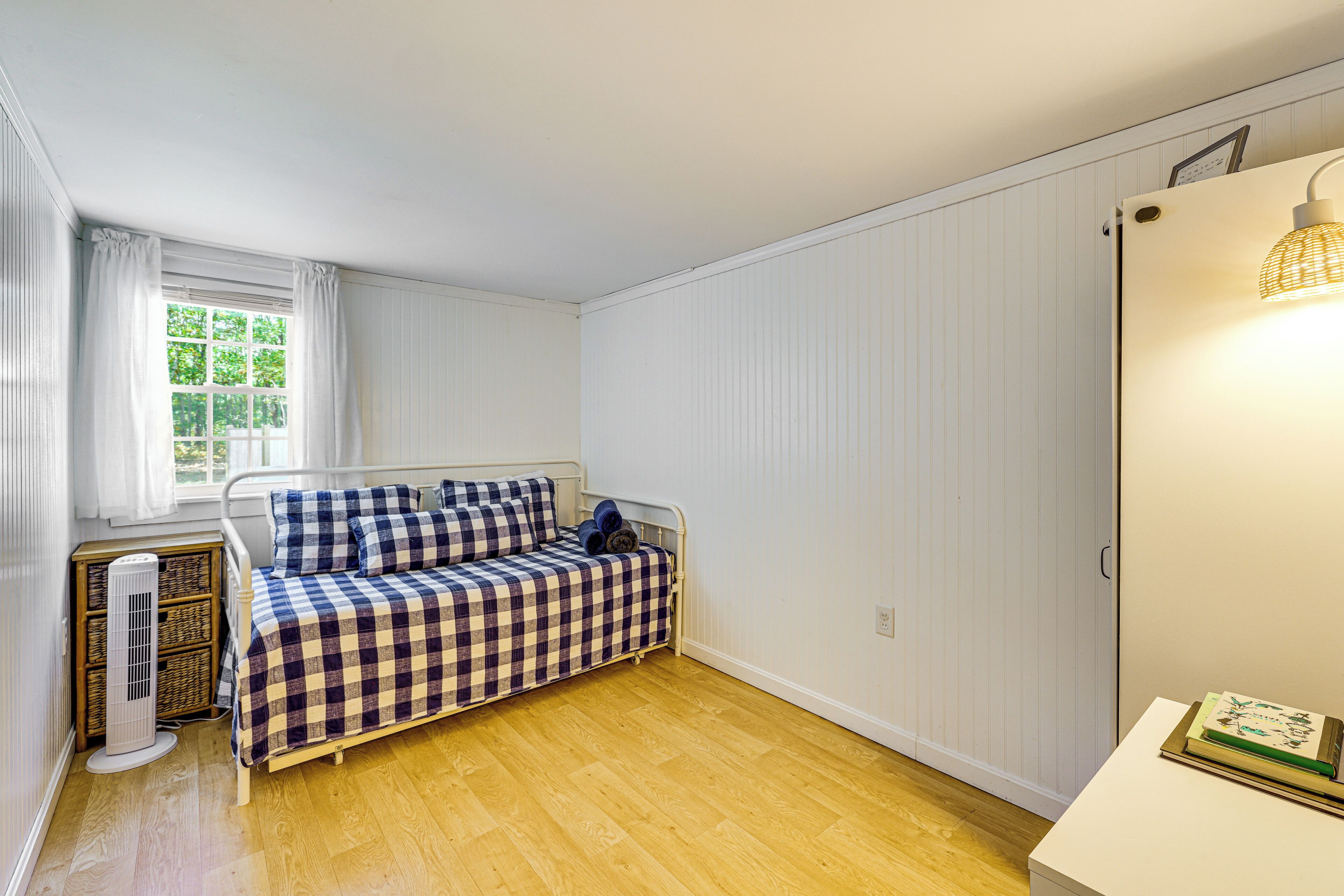 A small, neatly arranged bedroom with a single bed, a bedside table, a radiator, and a window with curtains.