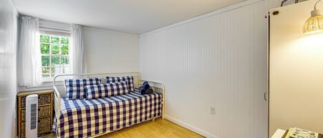 A small, neatly arranged bedroom with a single bed, a bedside table, a radiator, and a window with curtains.