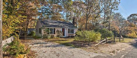 A house with a front porch, surrounded by trees and a gravel driveway.