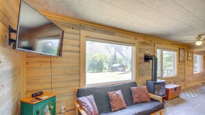 Een gezellig chaletinterieur met een bank, een aan de muur bevestigde televisie en een houtkachel.