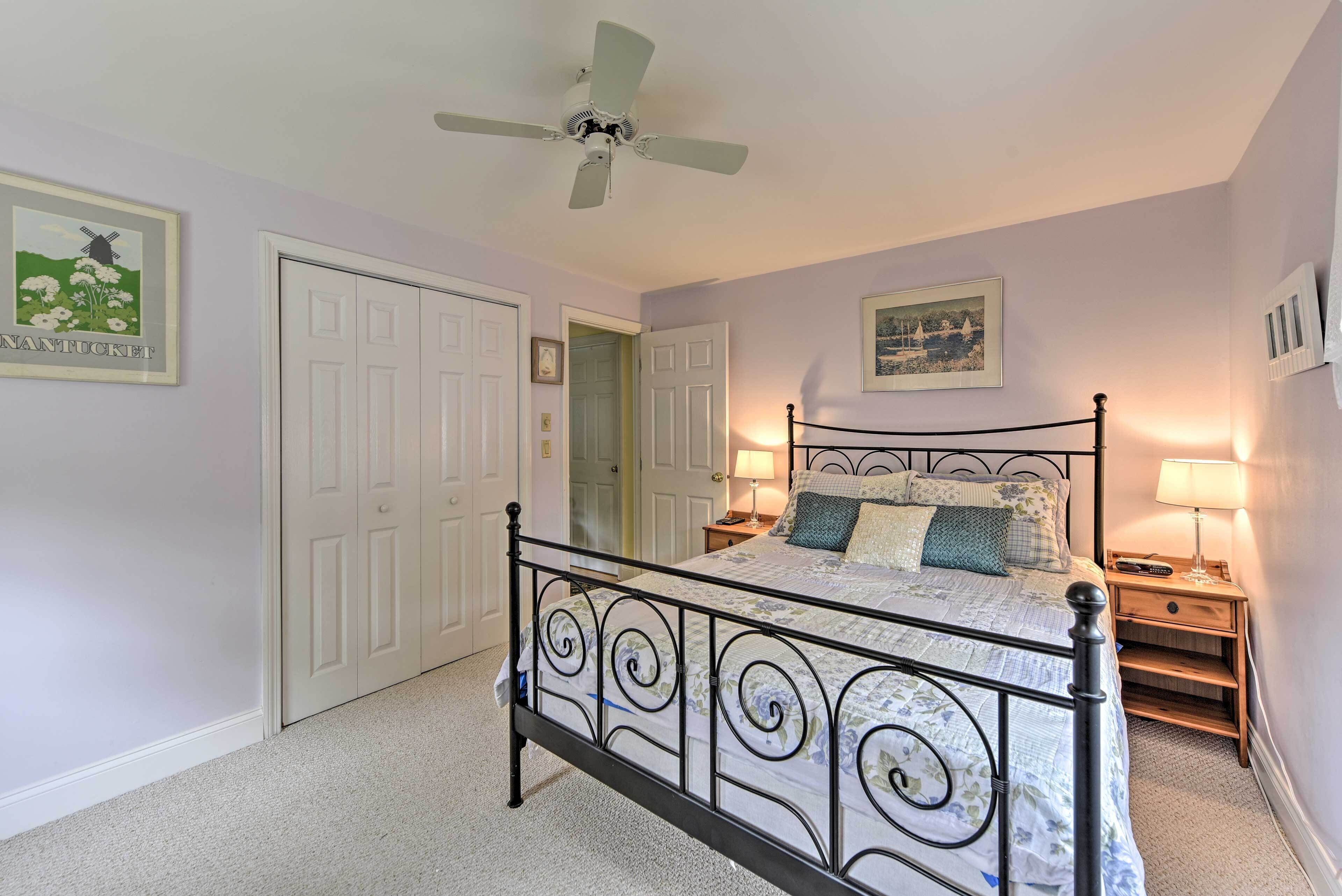 A bedroom with a four-poster bed, a ceiling fan, two bedside tables with lamps, and a door leading to another room.