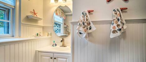 Un baño con un tocador blanco, un espejo, una decoración con estrella de mar y dos toallas colgadas en un perchero.
