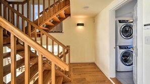 A wooden staircase leading to a second floor, a laundry room with two washing machines, and a light switch on the wall. - Multi-level Marion House: Loft, Deck + Ocean Views (Marion)
