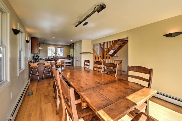 A spacious dining area with a large wooden table and multiple chairs, a kitchen in the background, and a staircase leading to another level.