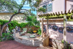 A stone-built outdoor seating area with a pergola, surrounded by lush greenery and a wooden fence. - Exotic Home w/ Patio & Grill: Walk to Canyon Lake! (Canyon Lake)