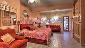Un dormitorio con cama, sofá rojo, armario de madera y un espejo grande.