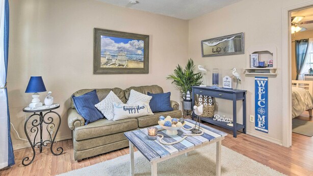 Een woonkamer met een beige bank, een bijzettafeltje, een schilderij van een strand in een lijst, een bord met de tekst 'Welkom' en een bord met de tekst 'Ontspan' op een console tafel.