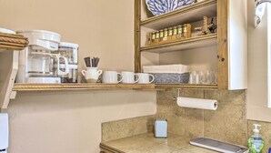 Een keuken met een koffiezetapparaat, mokken, een plank met potten, een handdoek en een zeepdispenser.