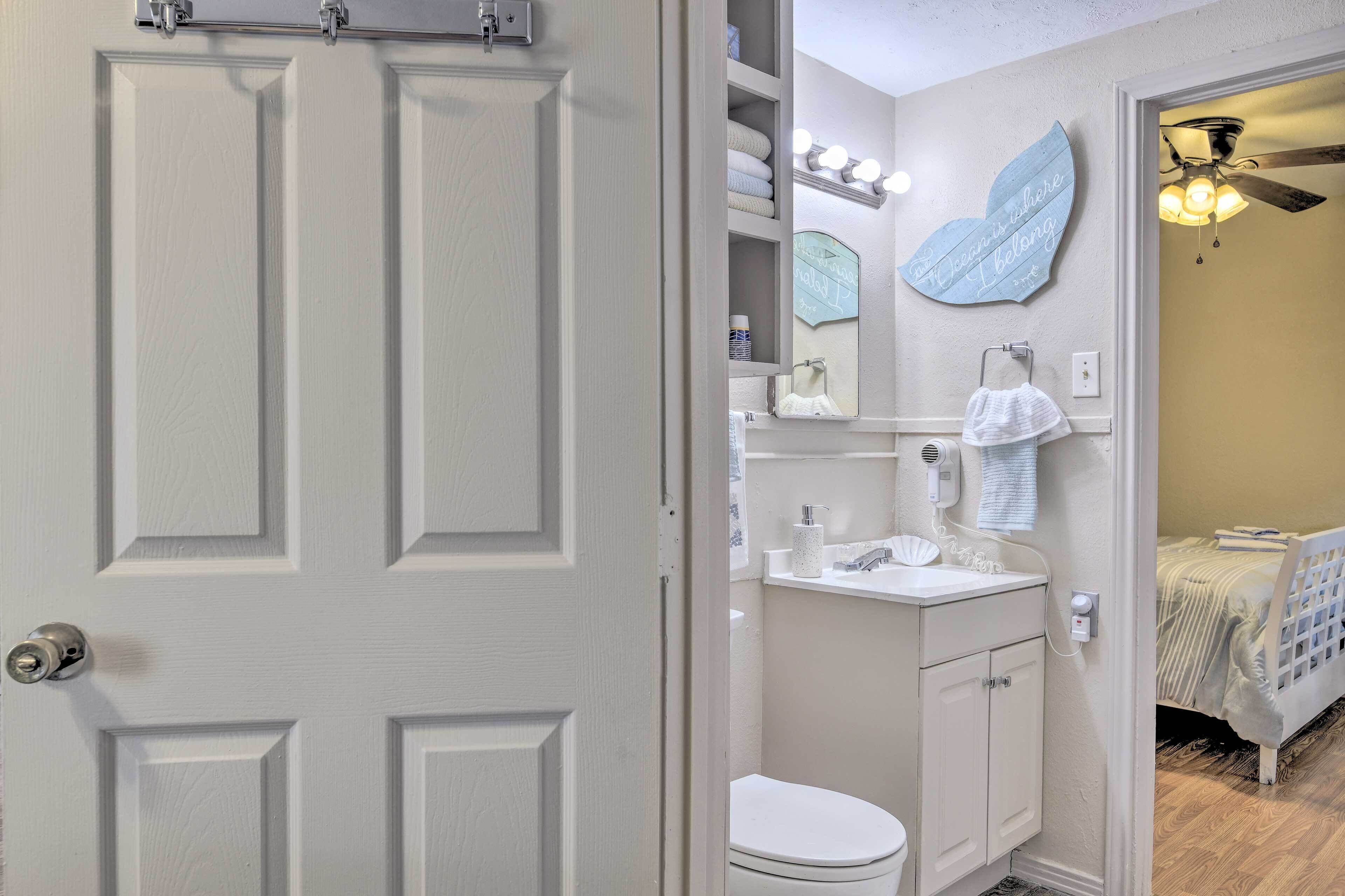 Ein Badezimmer mit Toilette, Waschbecken, Waschtisch und Spiegel. Ein Handtuch hängt an der Wand und ein Deckenventilator ist angebracht.