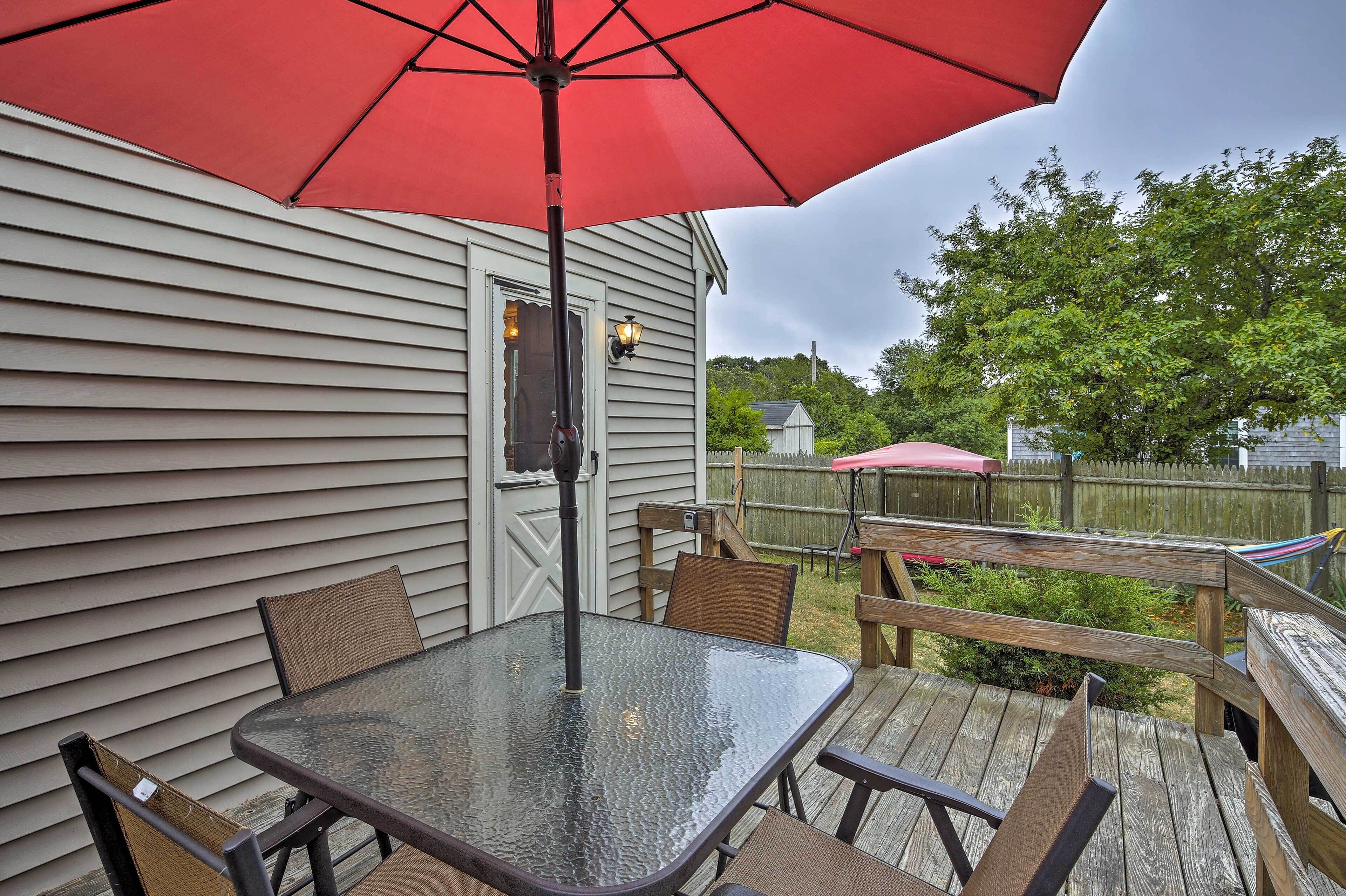 A glass table with chairs and a red umbrella on a wooden deck.