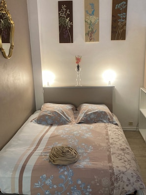 A neatly made bed with floral bedding, a vase with flowers, and wall art above. - ALBI-SUITE: Apartment in the heart of the city with free, private parking (Albi)