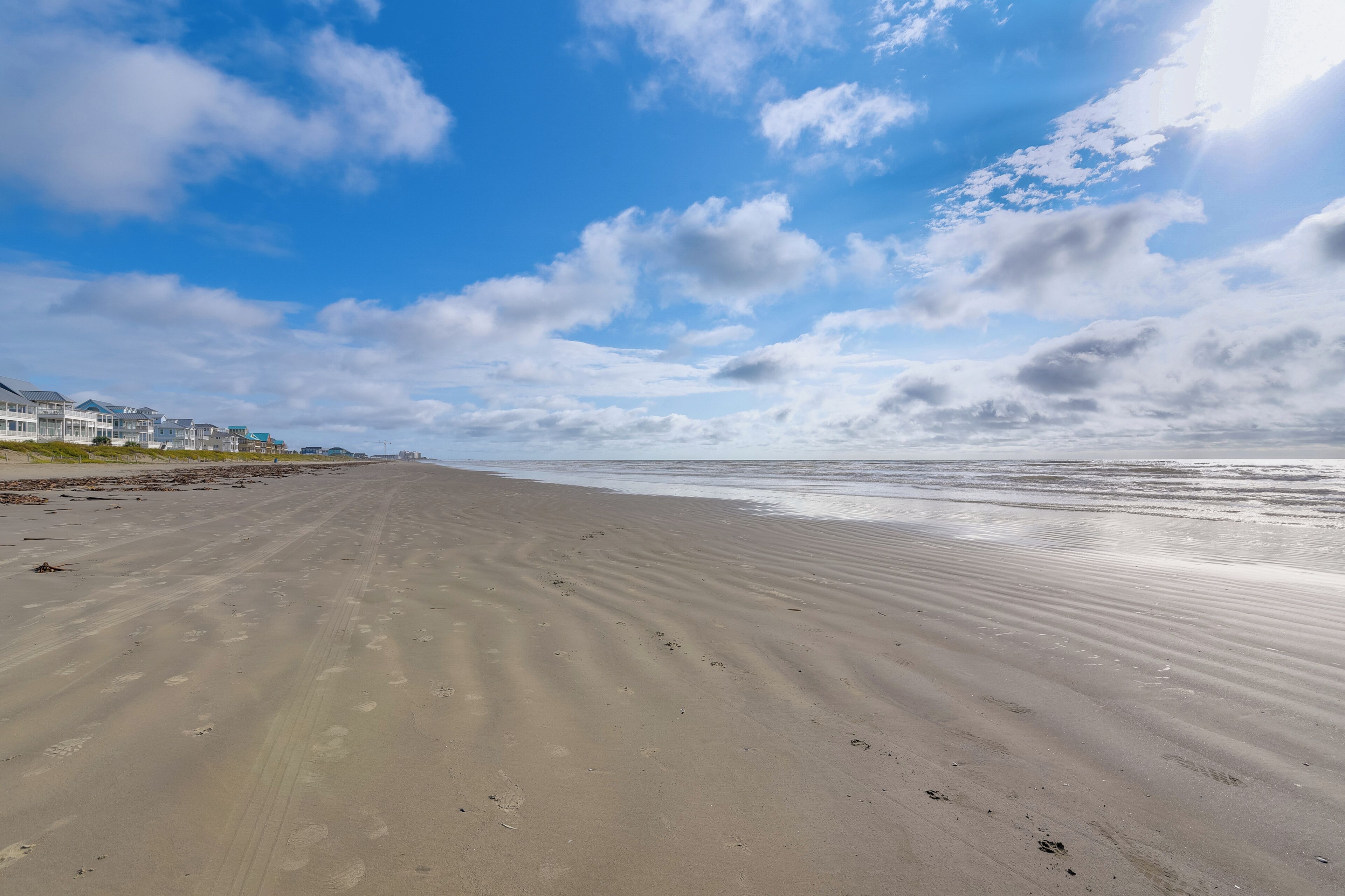 A wide sandy beach with footprints and a clear sky with clouds.