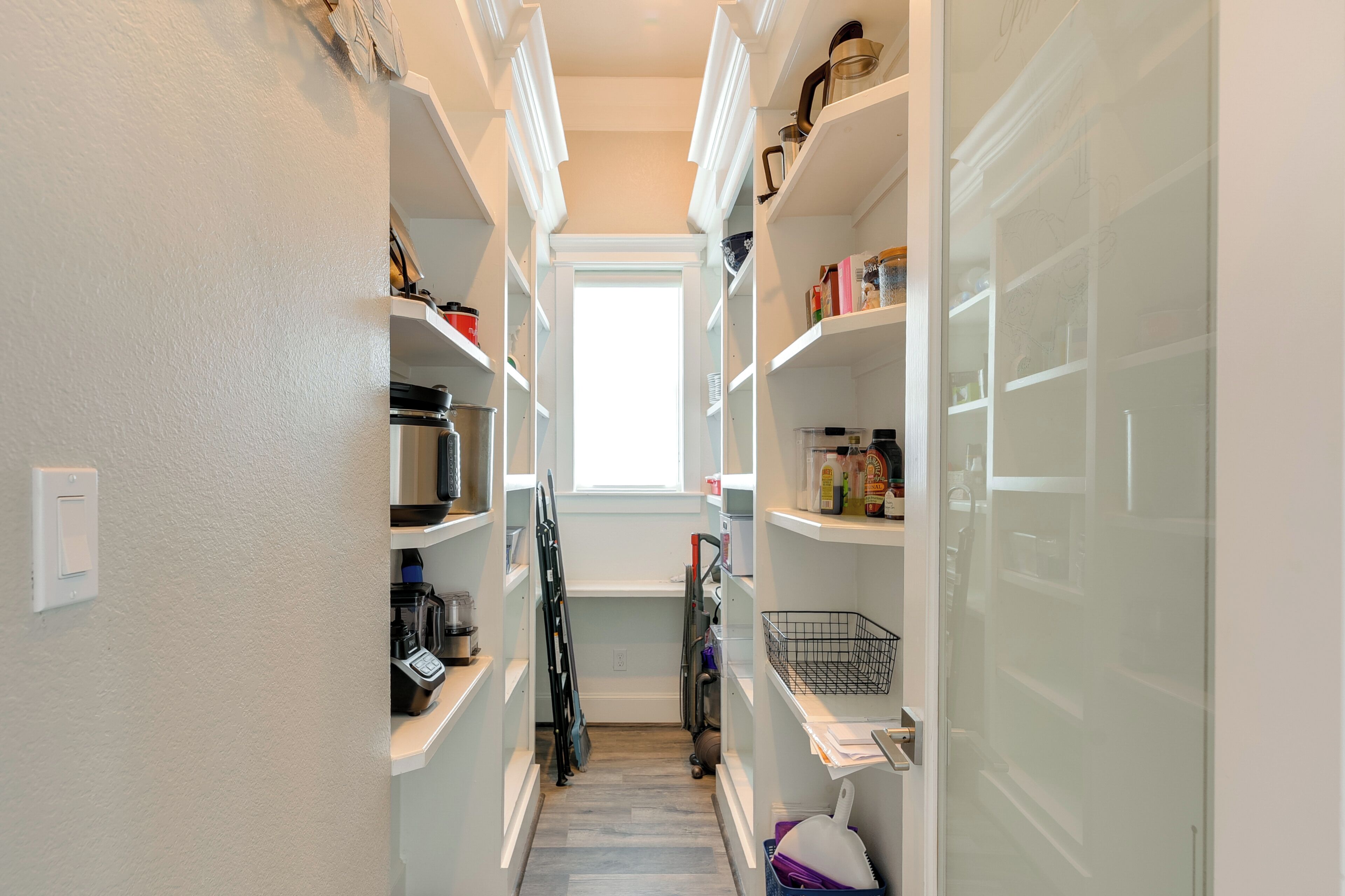 A narrow hallway with white shelving units on both sides, leading to a door at the end.