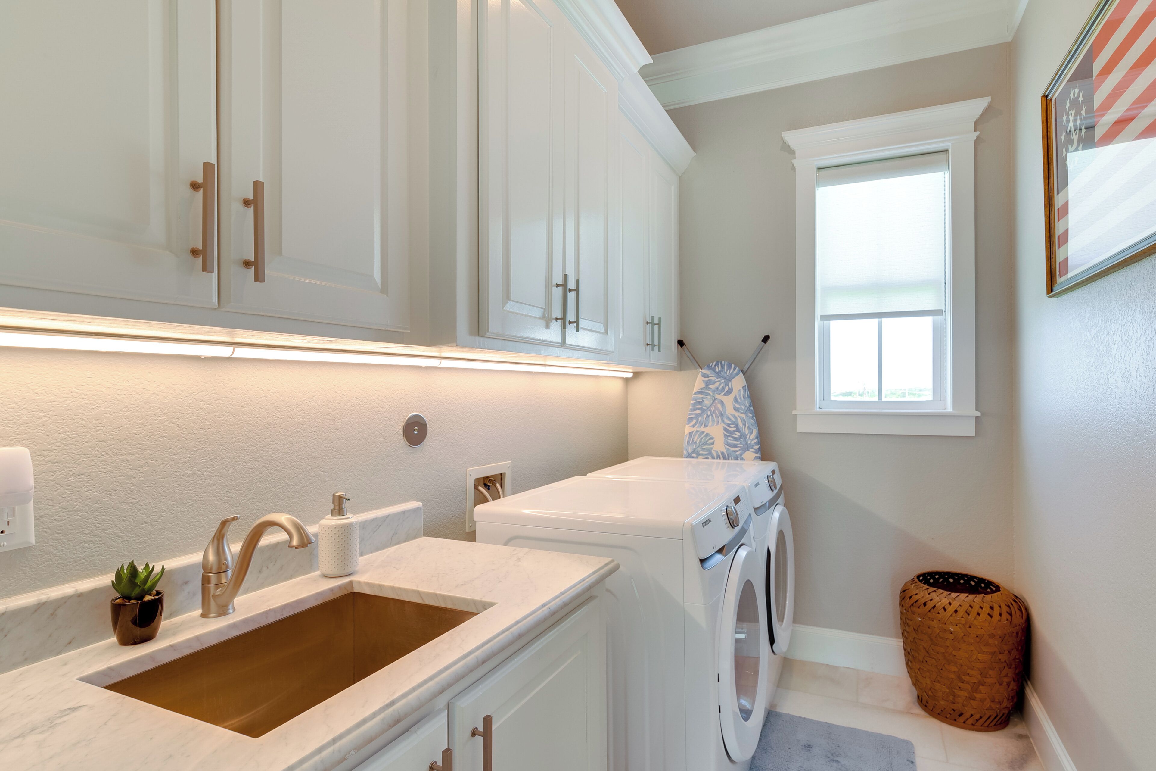 A laundry area with a washing machine, a sink with a faucet, and a window with blinds.