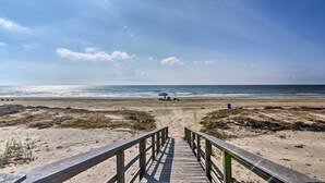 Un muelle de madera que conduce a una playa, con un paraguas azul y un carrito de golf.