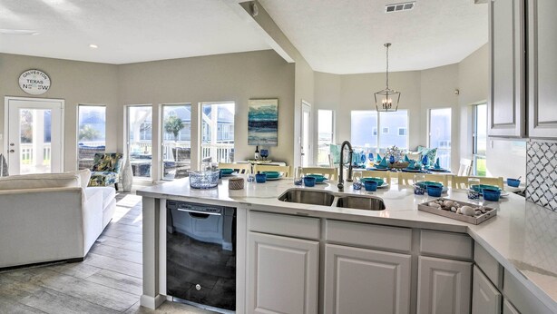 Una cocina amplia con armarios blancos, lavavajillas y una isla grande con fregadero. Varias ventanas ofrecen luz natural y vistas al exterior.