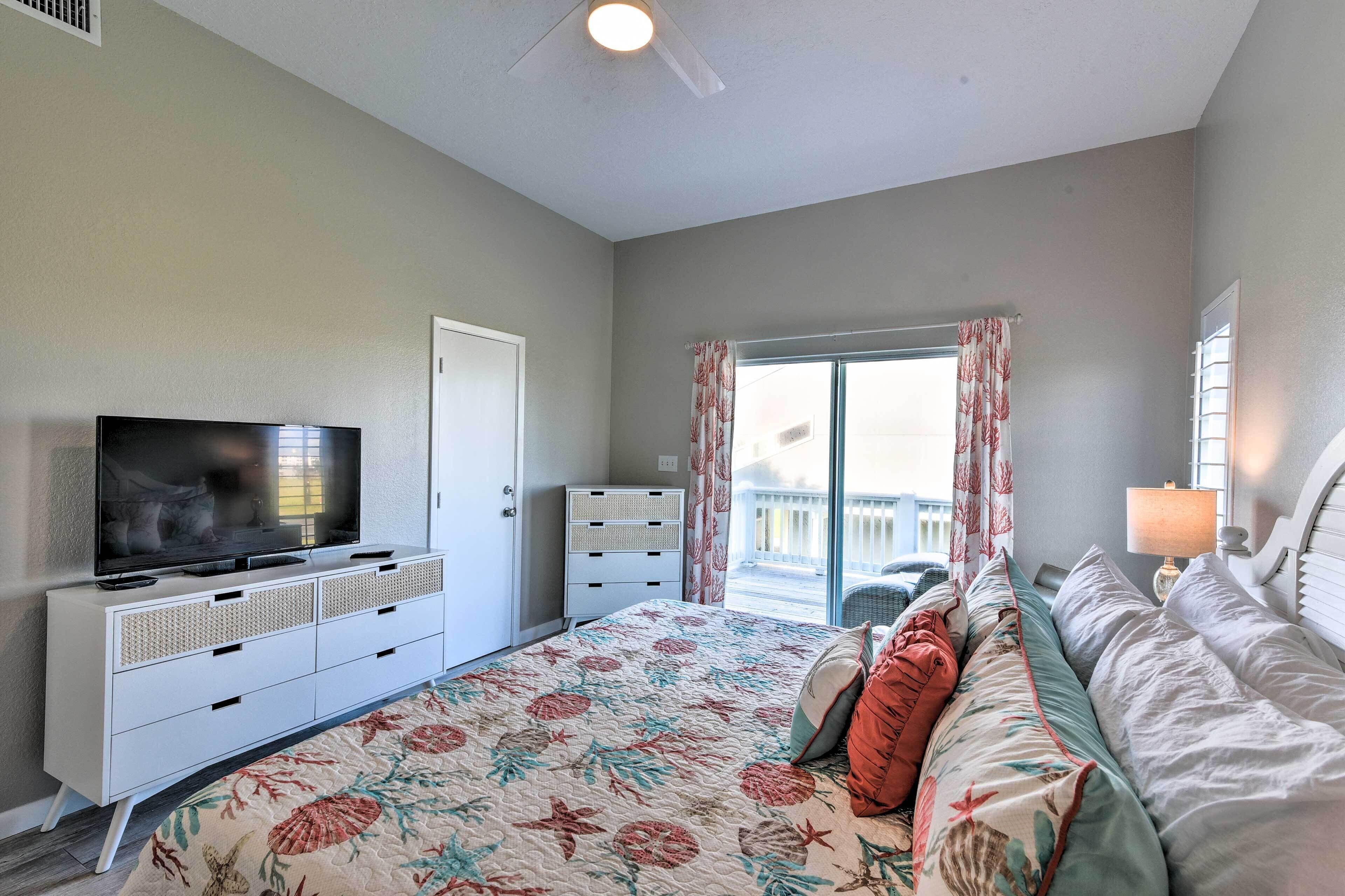 Une chambre à coucher avec un lit, un téléviseur posé sur une commode, une fenêtre avec des rideaux et un ventilateur de plafond.