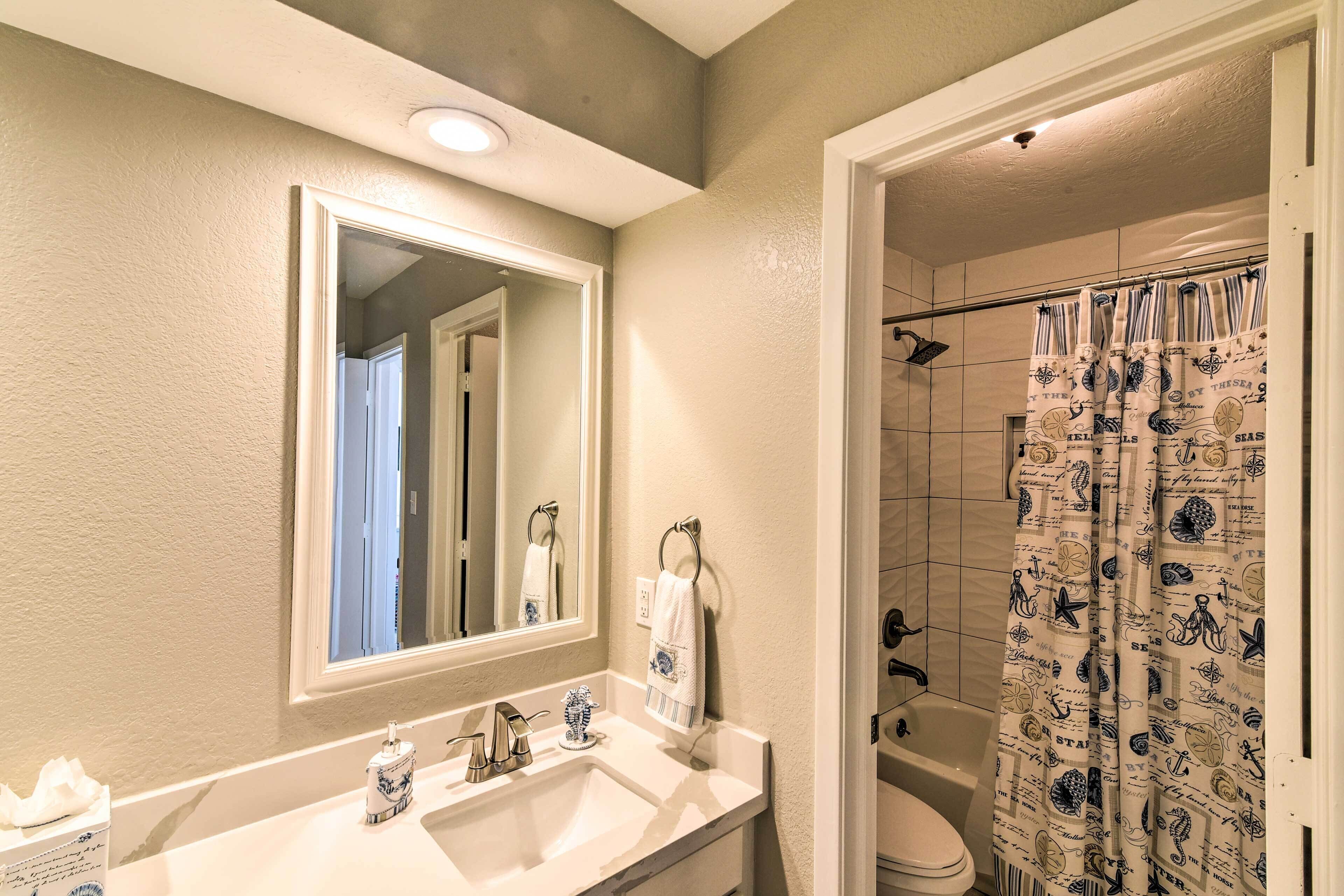 A bathroom with a sink, mirror, and shower curtain with nautical designs.