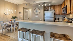 A kitchen with wooden cabinets, a stainless steel refrigerator, a white countertop, and a hanging light fixture. - Resort Pool, Gym & Hot Tub: Beachfront PCB Condo! (Panama City Beach)