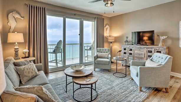 A spacious living room with a balcony, a ceiling fan, and a television on a wooden cabinet. - Resort Pool, Gym & Hot Tub: Beachfront PCB Condo! (Panama City Beach)