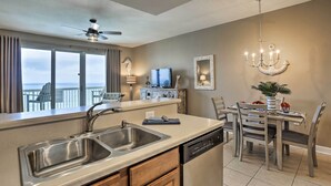 A modern kitchen with a dishwasher, double sink, and a dining area with a table and chairs. - Resort Pool, Gym & Hot Tub: Beachfront PCB Condo! (Panama City Beach)
