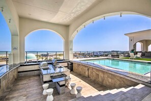 Un área de piscina en la azotea con bar, asientos y vistas al océano.