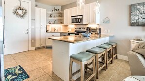 Een moderne keuken met witte kasten, een centraal eiland met krukken, een magnetron en een hangende lamp.