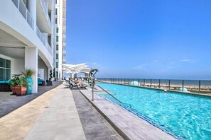 A poolside area with a clear view of the ocean, a pool, and a building with multiple balconies. - Beachfront Condo w/ Pool in Galveston! (Galveston)