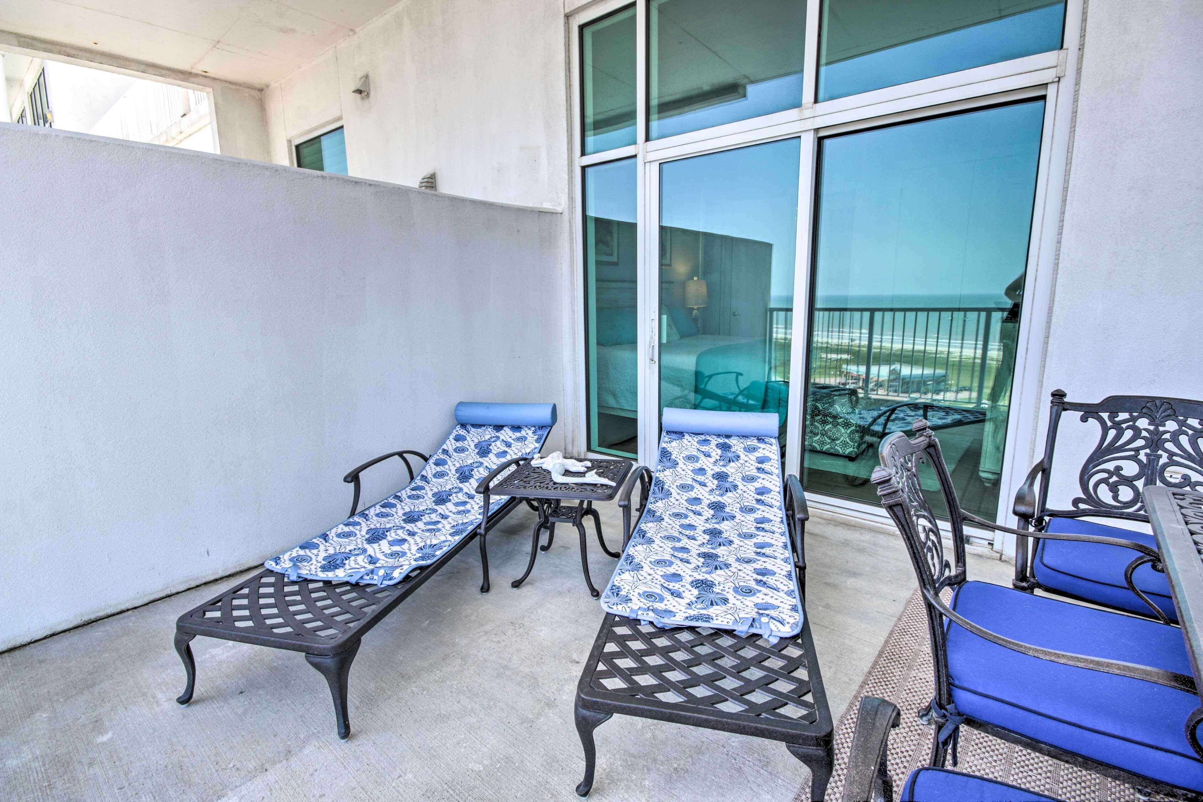 A balcony with two sun loungers and a table, overlooking a balcony with a view of the sea.
