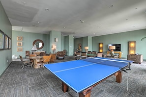 A spacious room with a ping pong table, comfortable seating, and a television. - Beachfront Condo w/ Pool in Galveston! (Galveston)