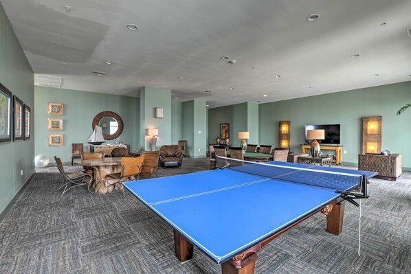 A spacious room with a ping pong table, comfortable seating, and a television. - Beachfront Condo w/ Pool in Galveston! (Galveston)