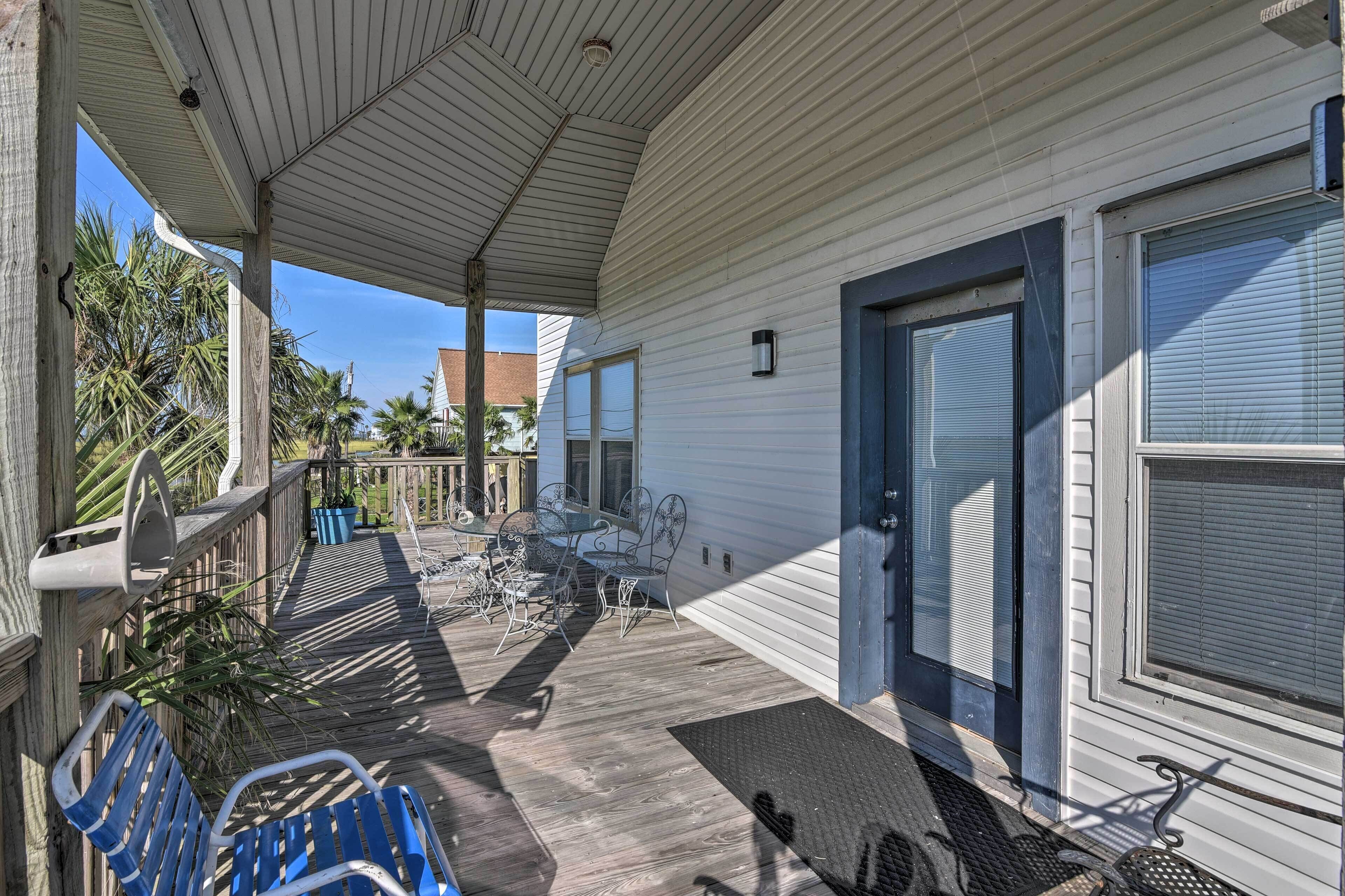 A covered porch with a wooden deck, metal chairs, and a table.