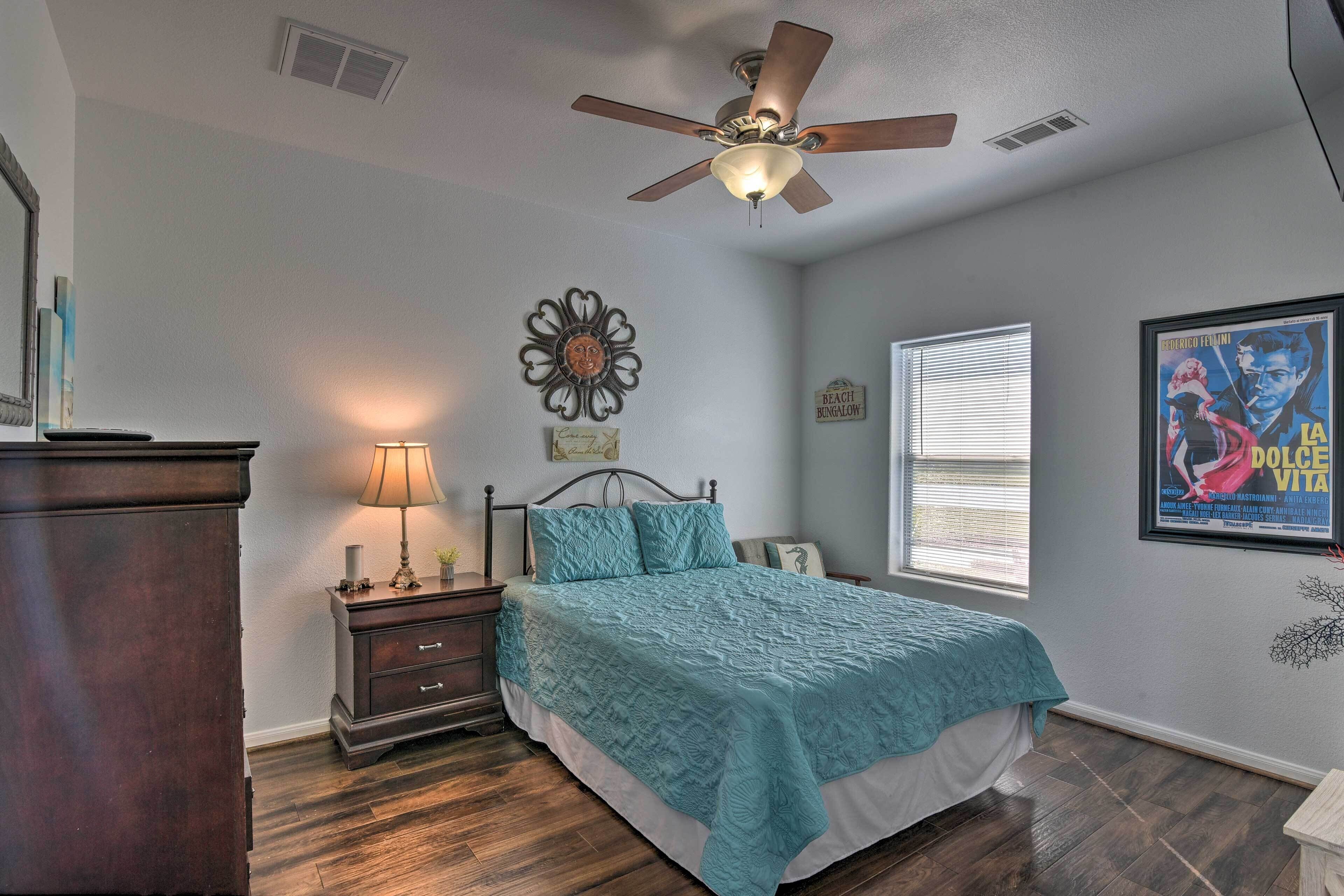 A bedroom with a bed, a nightstand, a dresser, a ceiling fan, a window with blinds, and a poster on the wall.
