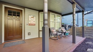 A covered porch with a wooden door, a welcome sign, and outdoor seating with cushions.