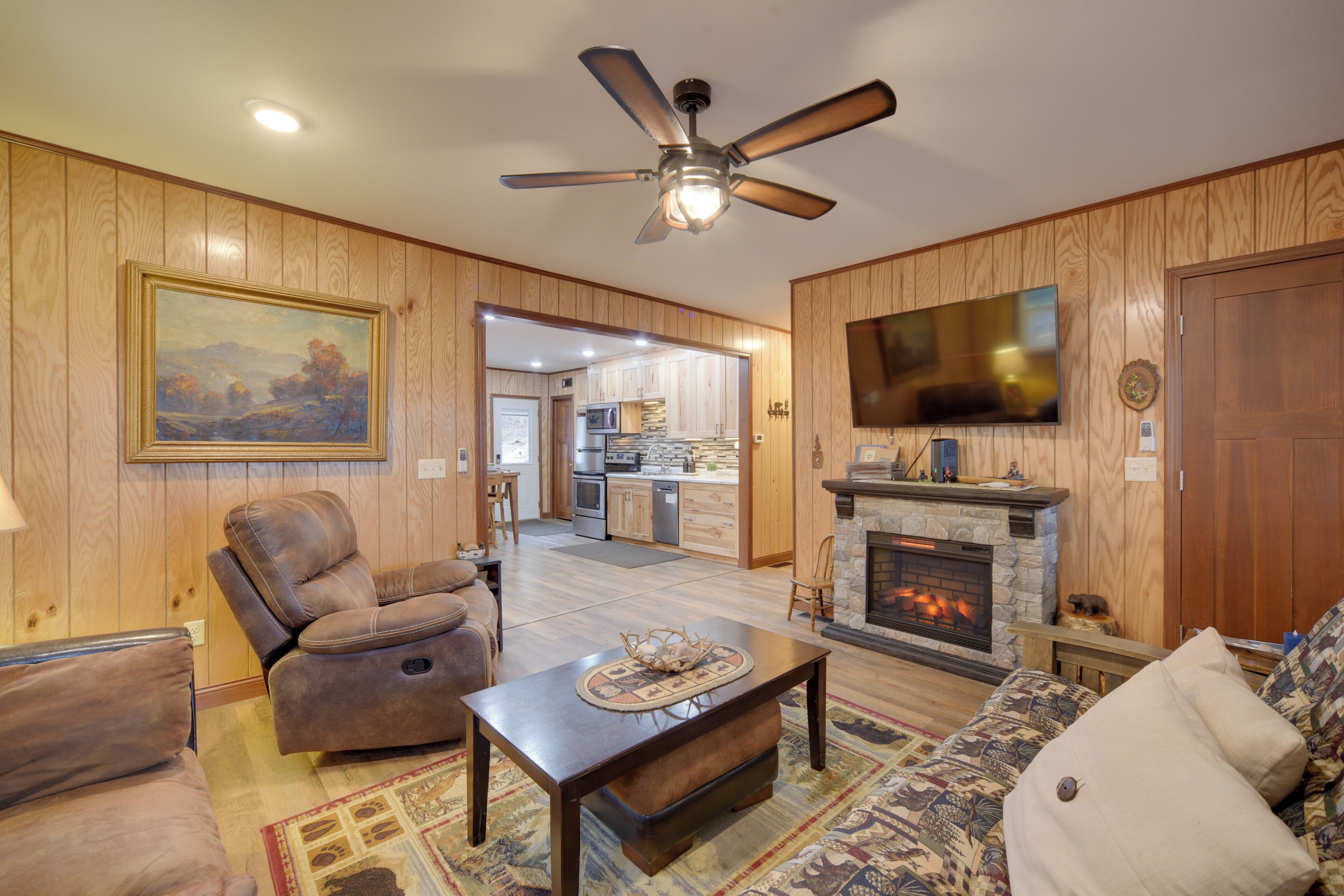 A living room with a fireplace, a ceiling fan, and a television mounted on the wall.