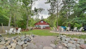 Une cabane rouge dotée d’une terrasse, entourée d’un chemin de gravier et d’une clôture en bois.