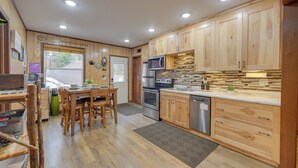 Une cuisine moderne avec des meubles en bois, des appareils électroménagers en acier inoxydable et un coin repas doté de chaises en bois.