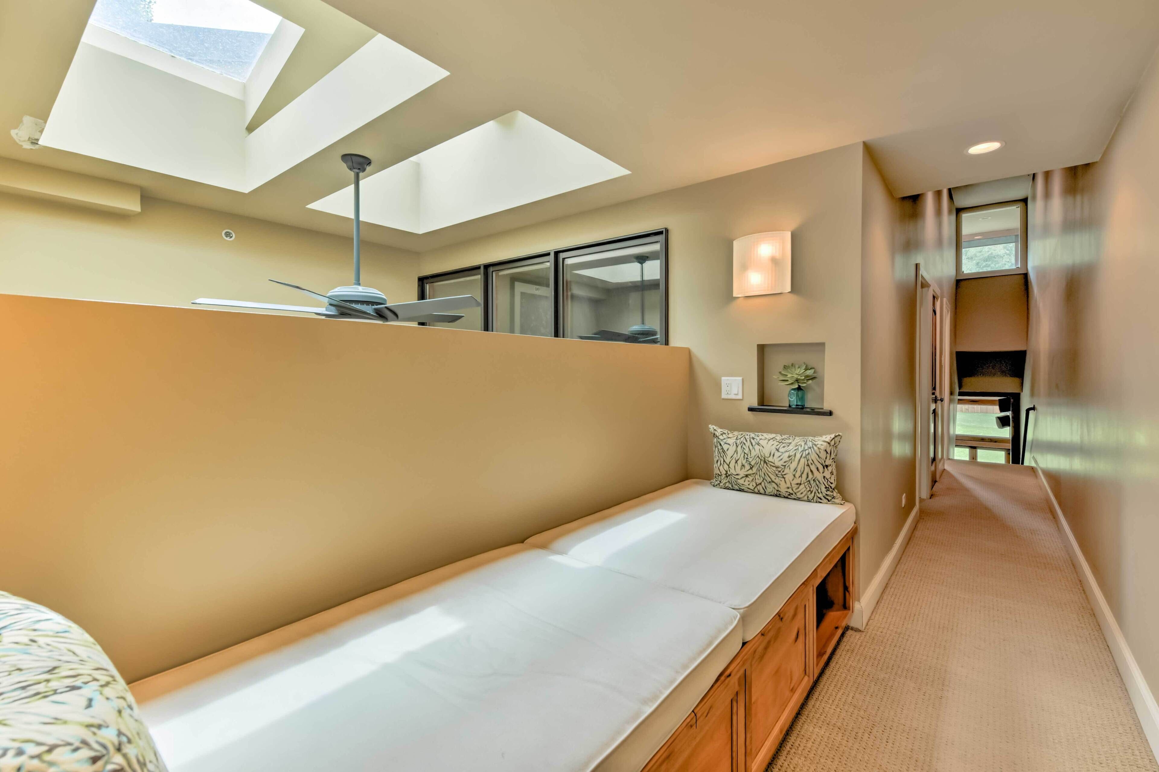 A modern hotel room with a skylight, a sofa, a desk, and a view of the hallway.