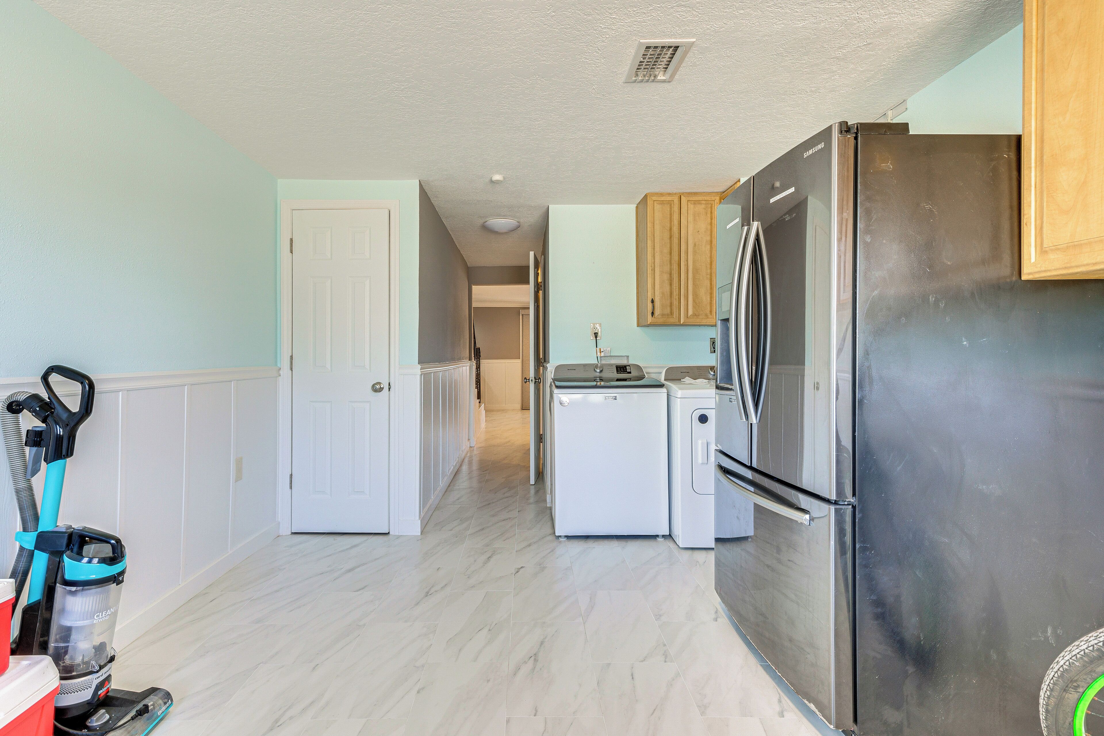 A kitchen with a stainless steel refrigerator, a washing machine, and a vacuum cleaner.