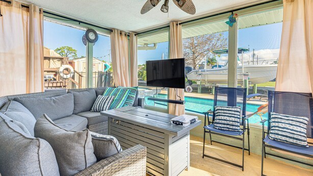 A modern outdoor living area with a sofa, chairs, a TV, and a pool view. - Spacious Canalfront Home w/ Pool ~ 1/2 Mi to Beach (Hudson)