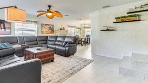 A modern living room with a sectional sofa, a wooden coffee table, and a ceiling fan. - Spacious Canalfront Home w/ Pool ~ 1/2 Mi to Beach (Hudson)