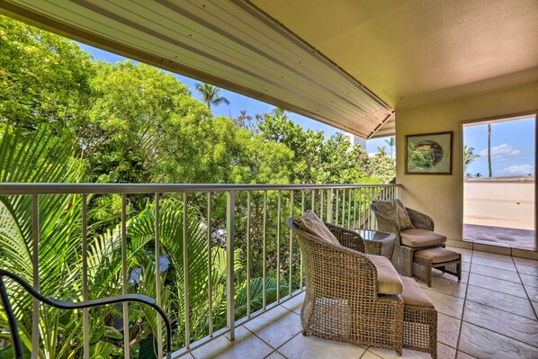 A balcony with wicker furniture and a view of lush greenery.