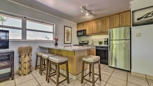 A modern kitchen with wooden cabinets, a stainless steel refrigerator, a microwave, and a bar area with stools.