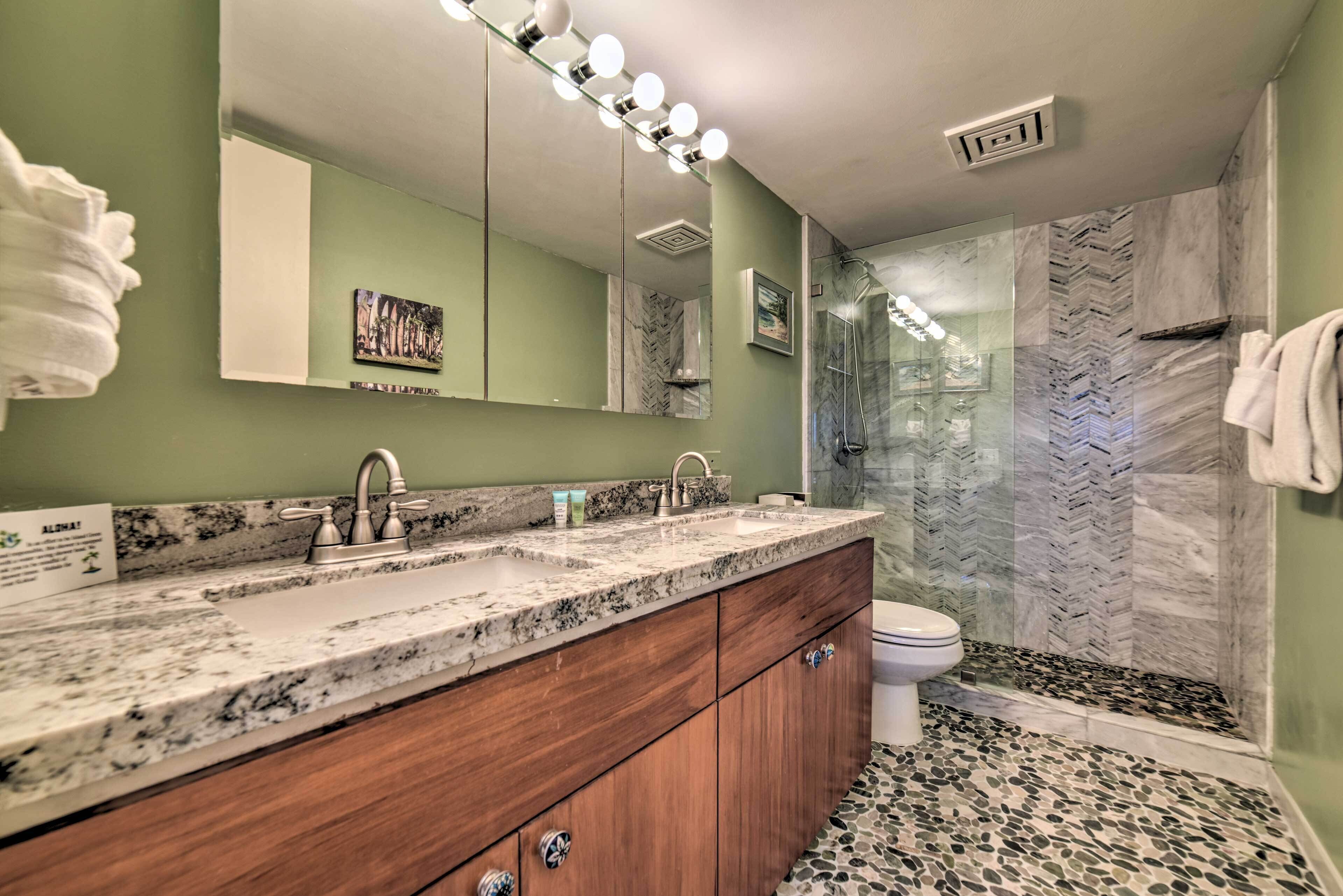 A bathroom with a granite countertop, wooden cabinets, a double sink, and a glass shower enclosure.