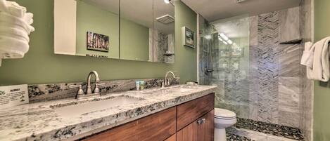 A bathroom with a granite countertop, wooden cabinets, a double sink, and a glass shower enclosure.