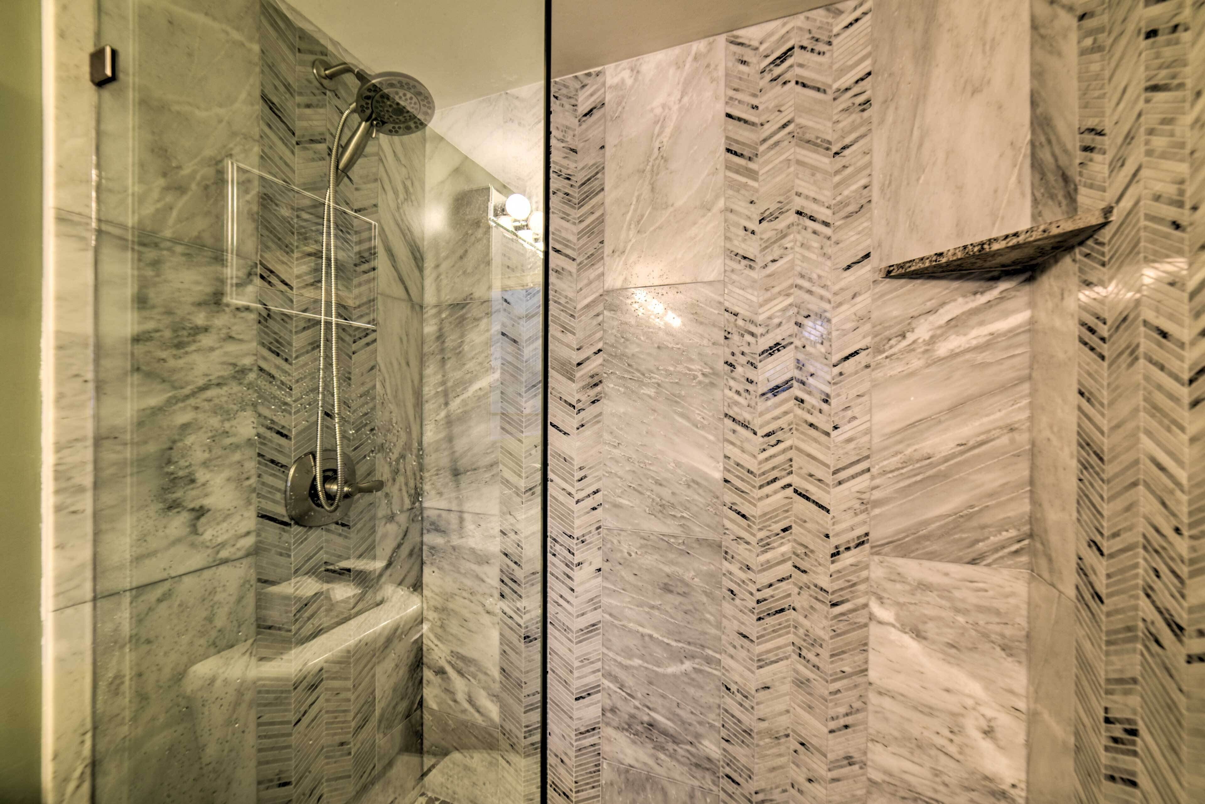 A shower with a glass door and a herringbone marble wall.