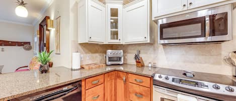 A kitchen with white cabinets, a granite countertop, a built-in oven, a microwave, and a dishwasher.